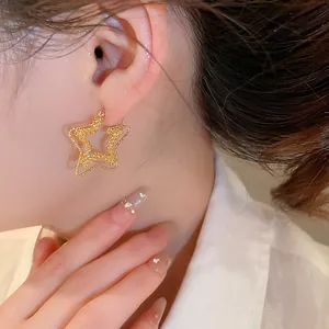 Close-up detail of elegant textured 18k gold plated star stud earrings worn on person's ear