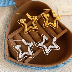Macro view of textured star-shaped earrings in gold and silver within a heart box