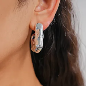 Close-up of irregular silver-tone metal earring with crinkled texture on ear