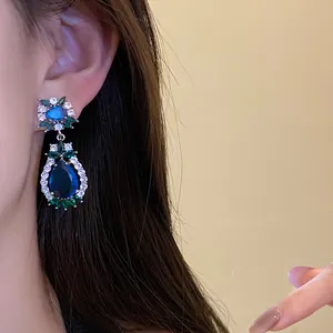 Nahaufnahme von eleganten Vintage-Blumen-Ohrhängern mit blauen und grünen Zirkonia am Modell