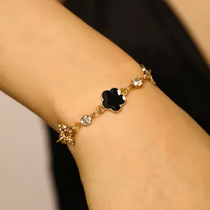 Gros plan d'un bracelet doré avec trèfle à cinq feuilles noir et breloques étoiles