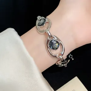 Gros plan d'un bracelet ovale argenté avec des strass gris foncé porté au poignet.