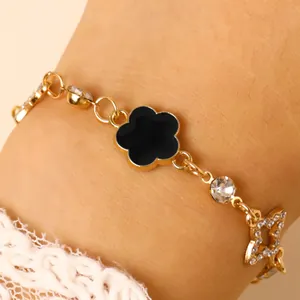 Détail d'un bracelet doré avec trèfle en émail noir et breloques étoiles en strass brillants