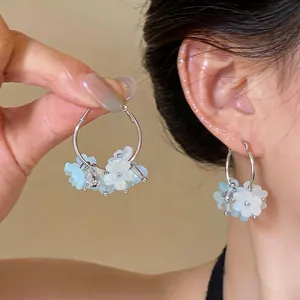 Macro detail view of sweet style blue and white resin flower hoop earrings on an ear
