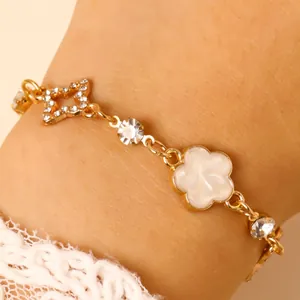 Détail d'un bracelet en chaîne dorée avec une étoile en strass et un trèfle en émail blanc