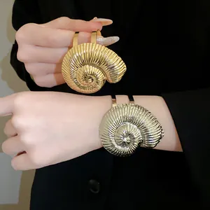 Détail de bracelets manchettes en métal doré et argenté en forme de nautile sur un modèle