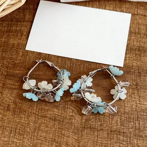 Macro detail of silver hoop earrings featuring blue and white resin flower charms