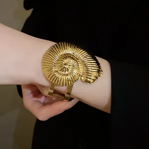 Gros plan d'un bracelet manchette ouvert en métal doré en forme de coquille de nautile.
