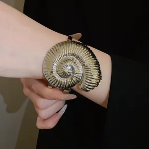 Vue détaillée du bracelet en forme de conque métallique avec texture plissée au poignet.