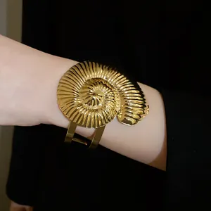 Vue rapprochée d'un bracelet manchette en forme de coquillage doré plissé au poignet