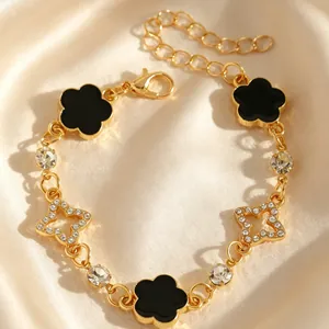 Détail d'un bracelet doré avec fleurs en émail noir et breloques en forme d'étoile.