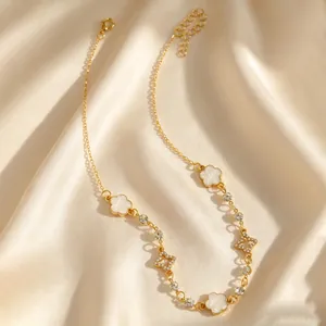 Détail du collier doré avec trèfle blanc et breloques étoiles en strass sur fond de satin.