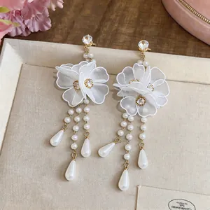 Close-up detail of elegant white mesh flower earrings with dangling pearl tassels.