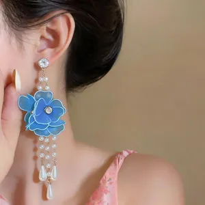 Close-up of elegant blue silk flower earrings with pearls and teardrop pendants on model