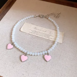 Close-up of beaded anklet with pink heart charms on a textured background