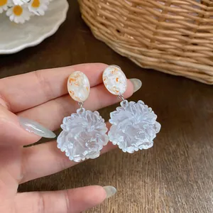 Close-up of white resin flower drop earrings with marble pattern oval studs.