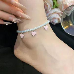 Detailed view of a beaded anklet featuring three pink heart charms on a person's ankle.