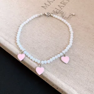 Close-up detail of white beaded anklet with three pink enamel heart charms