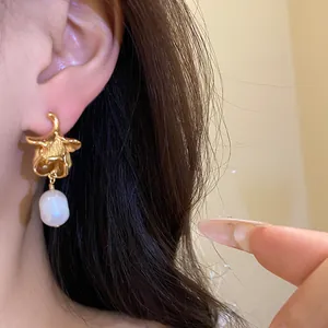 Close-up detail of a vintage-style gold flower earring with a dangling pearl on a model.