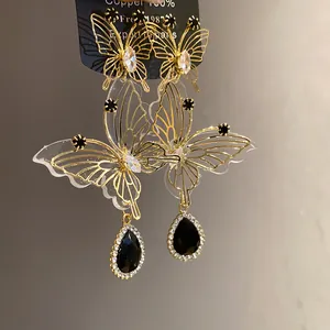 Exquisites Detail von goldenen hohlen Schmetterlingsohrringen mit schwarzen Tropfenanhängern