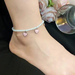 Detailed close-up shot of an elegant white beaded anklet with cute pink heart pendants