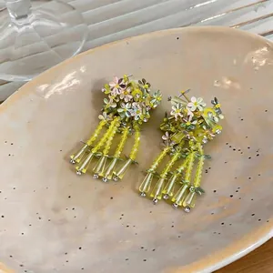 Korean style floral tassel earrings with yellow sequins and glass beads on a ceramic plate