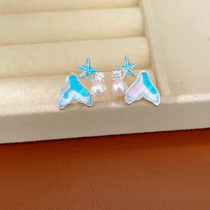 Primo piano di eleganti orecchini blu a forma di coda di sirena e stella marina con perle