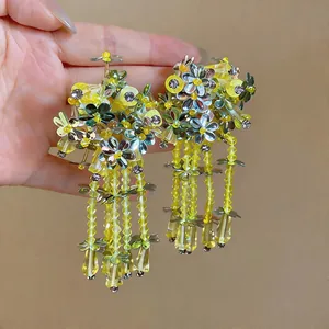 Close-up of vibrant yellow floral sequin earrings with long beaded tassels