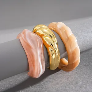 Vista dettagliata di bracciali rigidi in acrilico marmorizzato e oro su supporto grigio
