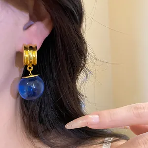 Dettaglio di orecchini vintage con cerchio dorato e ciondolo a sfera in resina blu