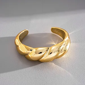 Primo piano di un bracciale rigido dorato lucido a spirale su uno sfondo neutro