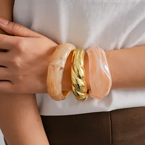 Dettaglio di bracciali rigidi in acrilico marmorizzato e bracciale a treccia dorato