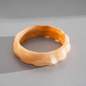 Dettaglio di un bracciale rigido in acrilico ambrato marmorizzato con design a onde