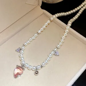 Close-up of pearl necklace with pink strawberry and heart charms in a beige jewelry box