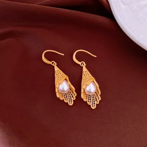 Elegant close-up view of golden lattice lace-work earrings with teardrop pearls on silk