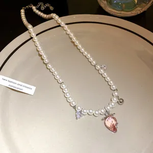 Close-up of elegant pearl necklace featuring a pink strawberry pendant on a ceramic plate.