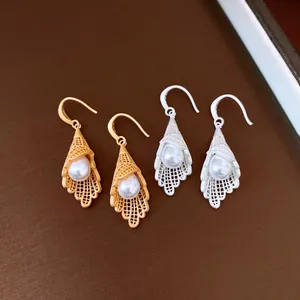 Detailed view of hollow lace cone earrings with white pearls in gold and silver finish