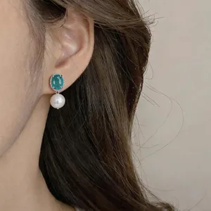 Dettaglio di eleganti orecchini a perno con zircone verde ovale e perla su modella