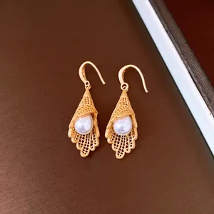 Close-up of gold filigree lace earrings with white pearl drops on brown base.