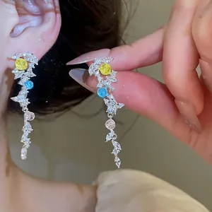 Vue détaillée de boucles d'oreilles pendantes avec zircons colorés jaunes et bleus.