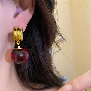 Primo piano di orecchini vintage dorati con ciondolo a sfera in resina rosso scuro