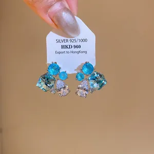 Gros plan de boucles d'oreilles géométriques en zircon bleu et clair sur carte en argent.