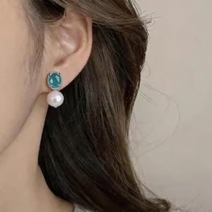 Primo piano di eleganti orecchini con zircone verde e perla indossati da una modella