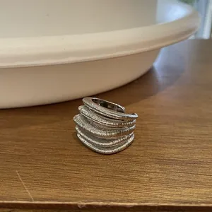 Detailed macro view of a silver-tone multi-layer textured open ring on a wooden surface