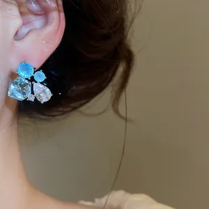 Gros plan de boucles d'oreilles clous en zircon géométrique avec pierres bleues et claires