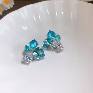 Gros plan de boucles d'oreilles géométriques en zircon bleu et clair dans un bol blanc