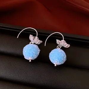 Close-up of light blue beaded ball earrings with silver flower detail on black leather surface.