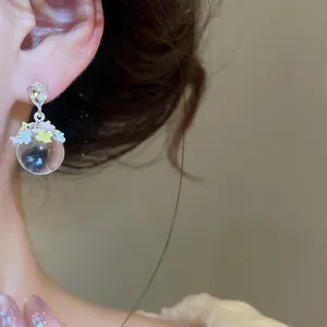 Vue détaillée de boucles d'oreilles clous en zircon avec pendentif boule de verre fleurie.
