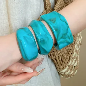 Detailed view of three turquoise marbled resin geometric open bangles worn on a wrist