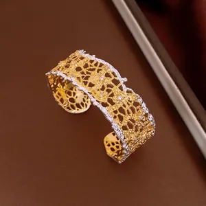 Close-up of elegant gold and silver lace-patterned hollow cuff bracelet with zircons
